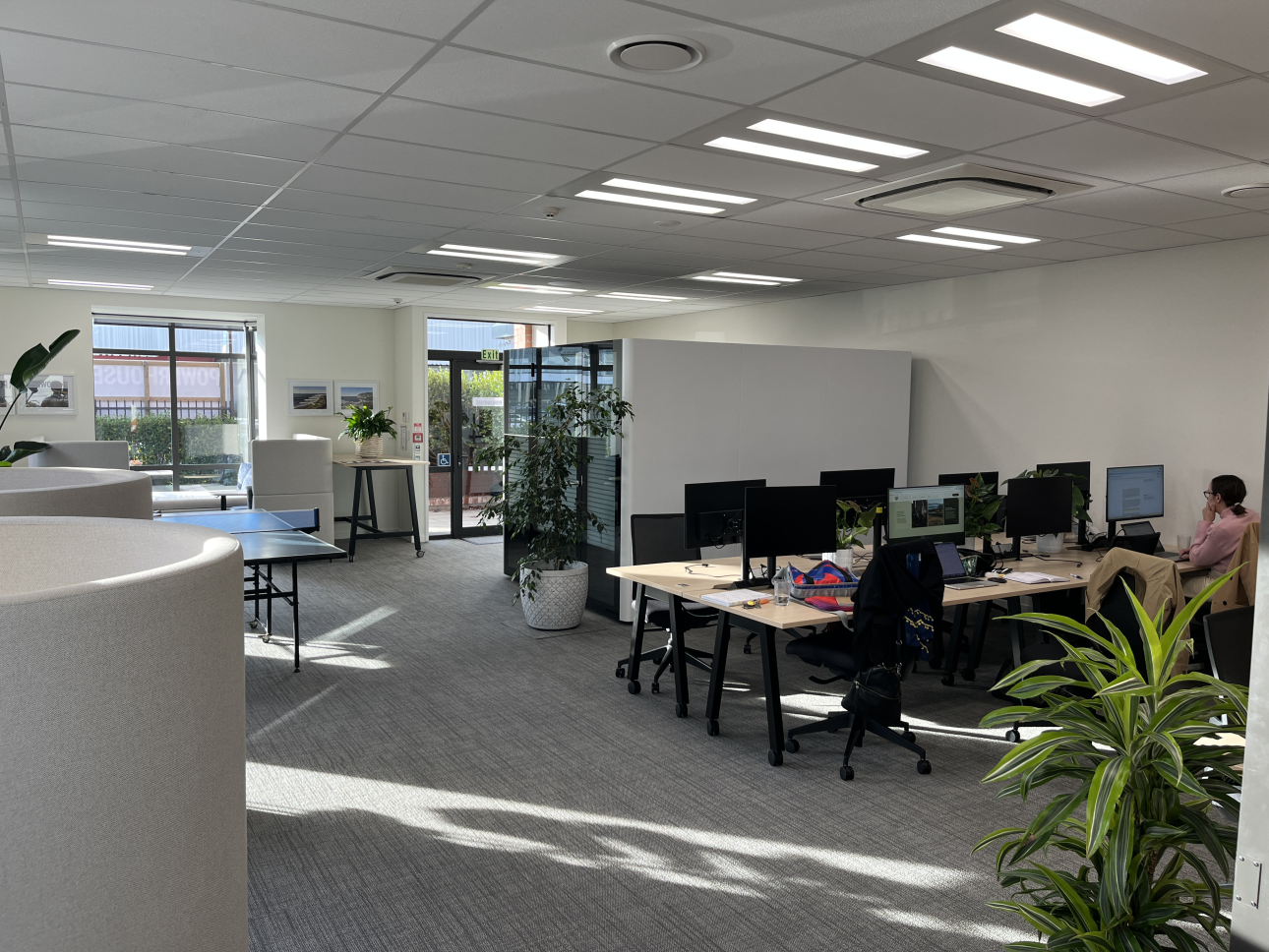 Hot desk area at Powerhouse Coworking with monitors, plants and natural light, and a member working at one of the desks